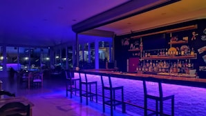 Zona de bar con una barra alargada, varias sillas y un fondo de pared de ladrillo.