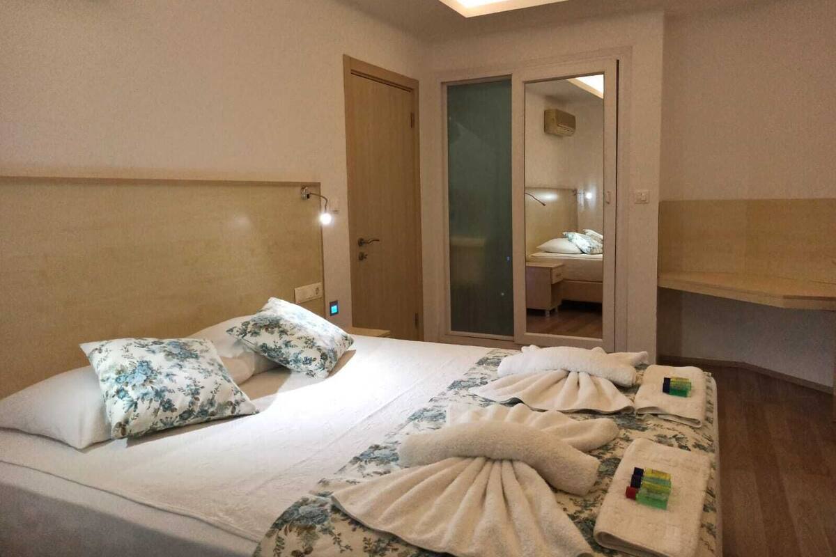 A hotel room with a bed, a mirror, a wardrobe, and a bedside table.
