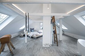 Une chambre de style loft moderne, dotée de fenêtres de toit, d’un lit, d’une échelle et d’un tabouret en bois.