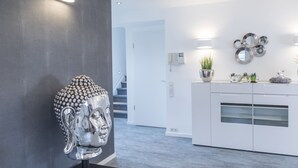 A modern interior with a Buddha head sculpture, a white kitchen with a plant, and a staircase. - Design-Studiowohnung in Gütersloh (Guetersloh)