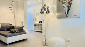 A modern living room with a white sofa, a floor lamp, a white pouf, and a painting of a bull's head. - Design-Studiowohnung in Gütersloh (Guetersloh)