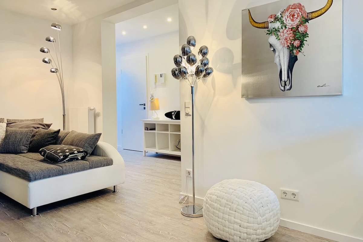 A modern living room with a white sofa, a floor lamp, a white pouf, and a painting of a bull's head.