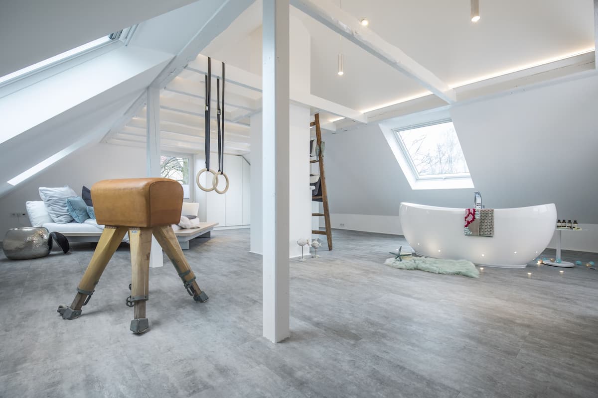 A modern, spacious room with a skylight, a large bathtub, and a tripod stool.