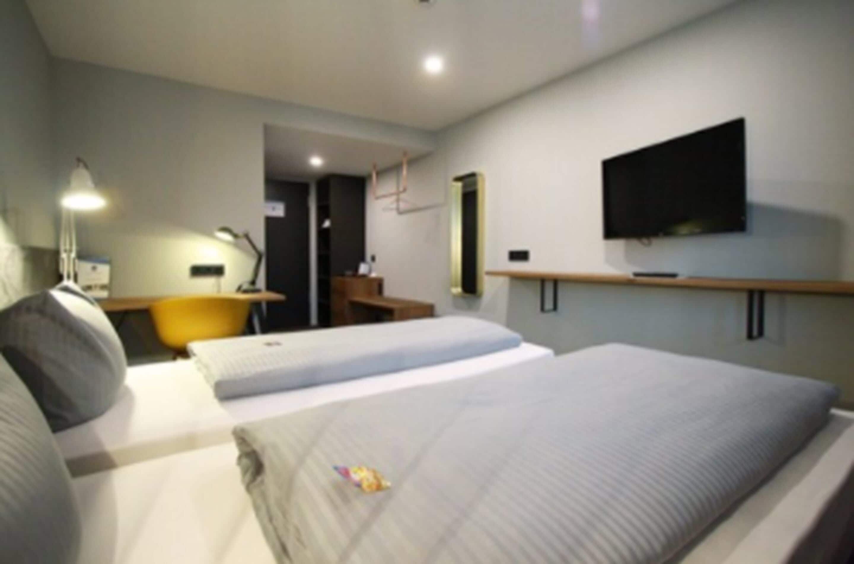 Habitación de hotel con dos camas, un escritorio, una silla, un televisor y una lámpara.