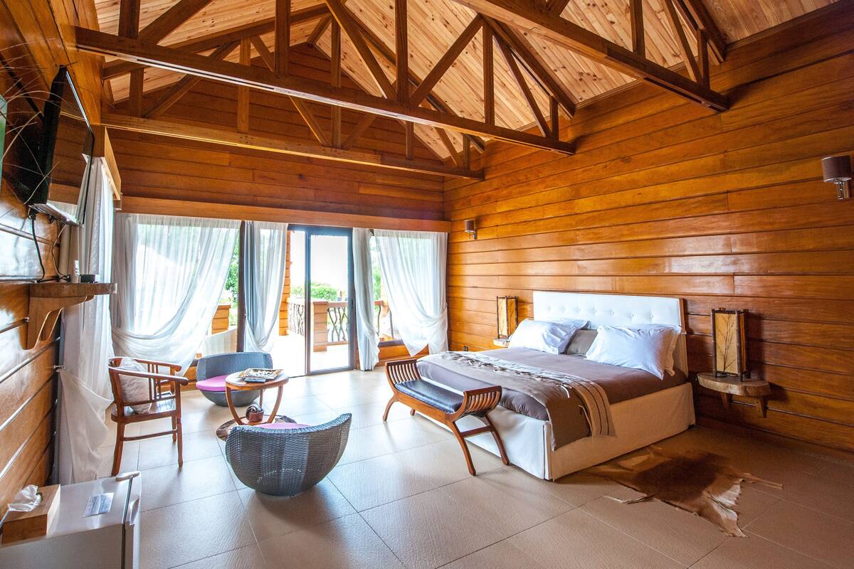 Quarto de cabana de madeira com uma cama, duas cadeiras, uma mesa e uma janela grande.