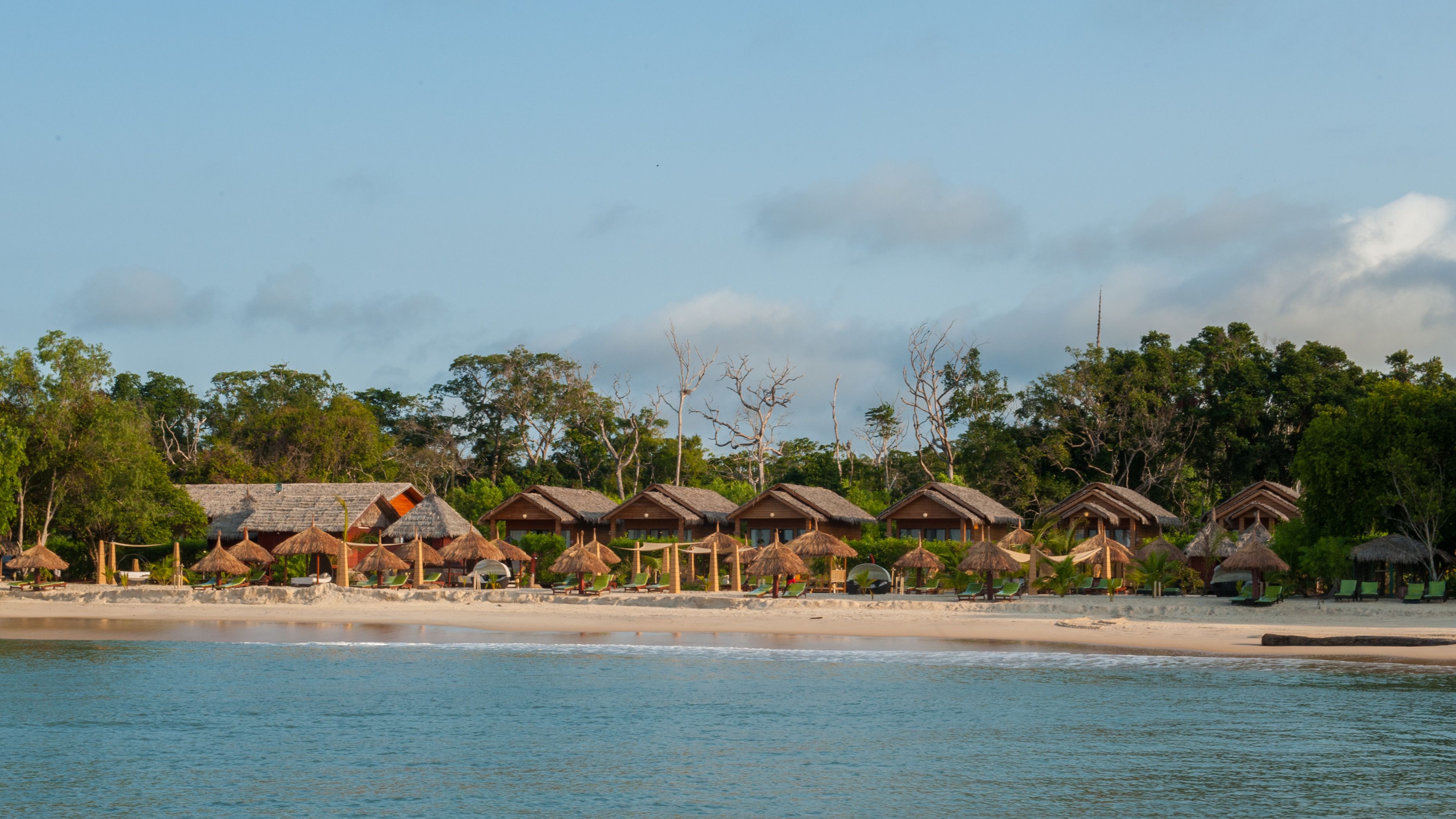 A beachfront resort with thatched-roof cabins and beachside seating.