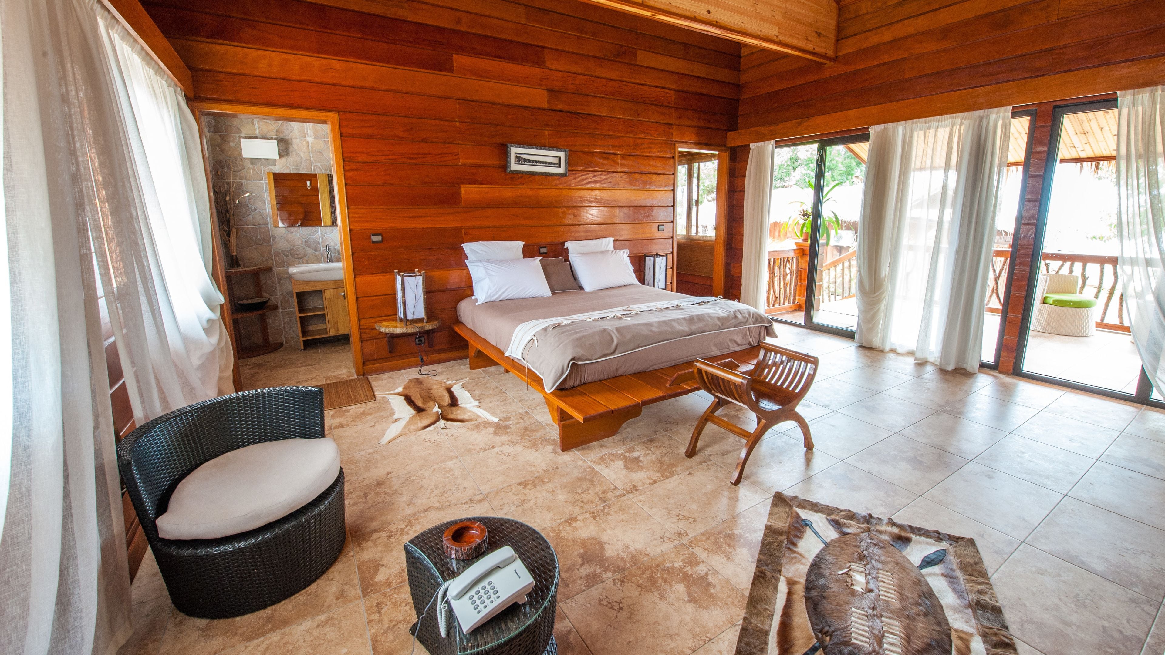 A spacious bedroom with a large bed, a wooden headboard, a sitting area with a chair, and a view of the outdoors.