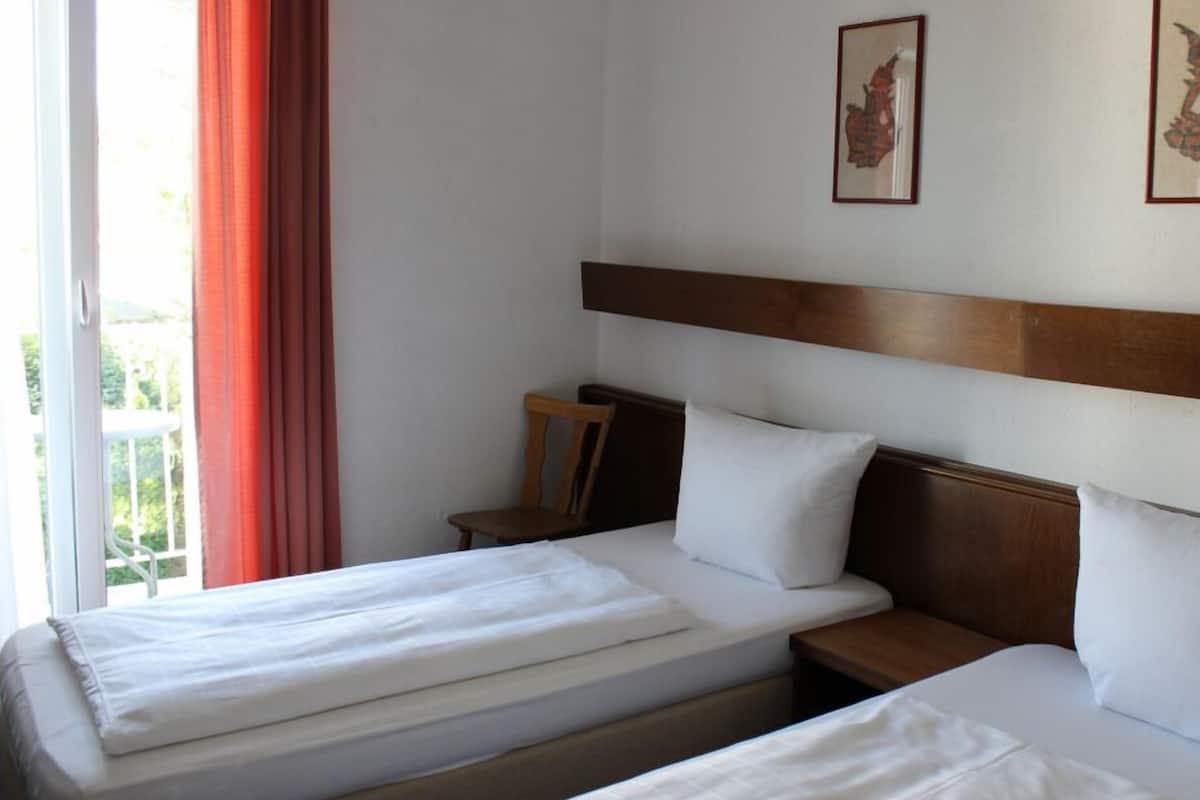A hotel room with two single beds, a wooden headboard, a small wooden chair, and two framed pictures on the wall.