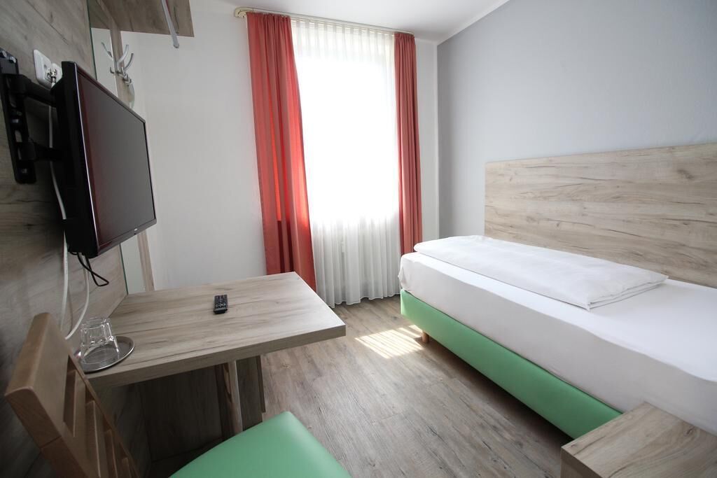 Une chambre d’hôtel avec un lit, un bureau, une télévision et une fenêtre avec des rideaux.