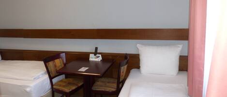 Habitación de hotel con dos camas individuales, una mesa de madera con un control remoto y dos sillones tapizados.