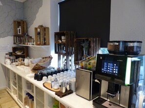 Montaje tipo buffet con máquina de café, dispensadores de condimentos y diferentes alimentos.
