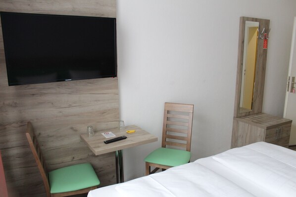 Una habitación de hotel con una cama, un escritorio con silla, un televisor montado en la pared y un espejo.