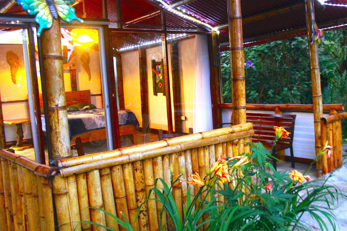 Un espace extérieur aménagé avec des meubles en bambou, comprenant une table et des chaises, le tout entouré d’une végétation luxuriante et de fleurs.
