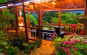 An outdoor wooden structure with a fire feature, surrounded by lush greenery and potted plants. - Refugio Puente Explanacion Ecolodge (Salento)