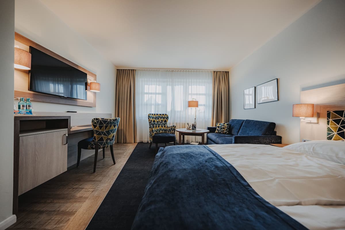 Ett hotellrum med en säng, ett skrivbord, en TV, en stol, en soffa och ett litet bord.