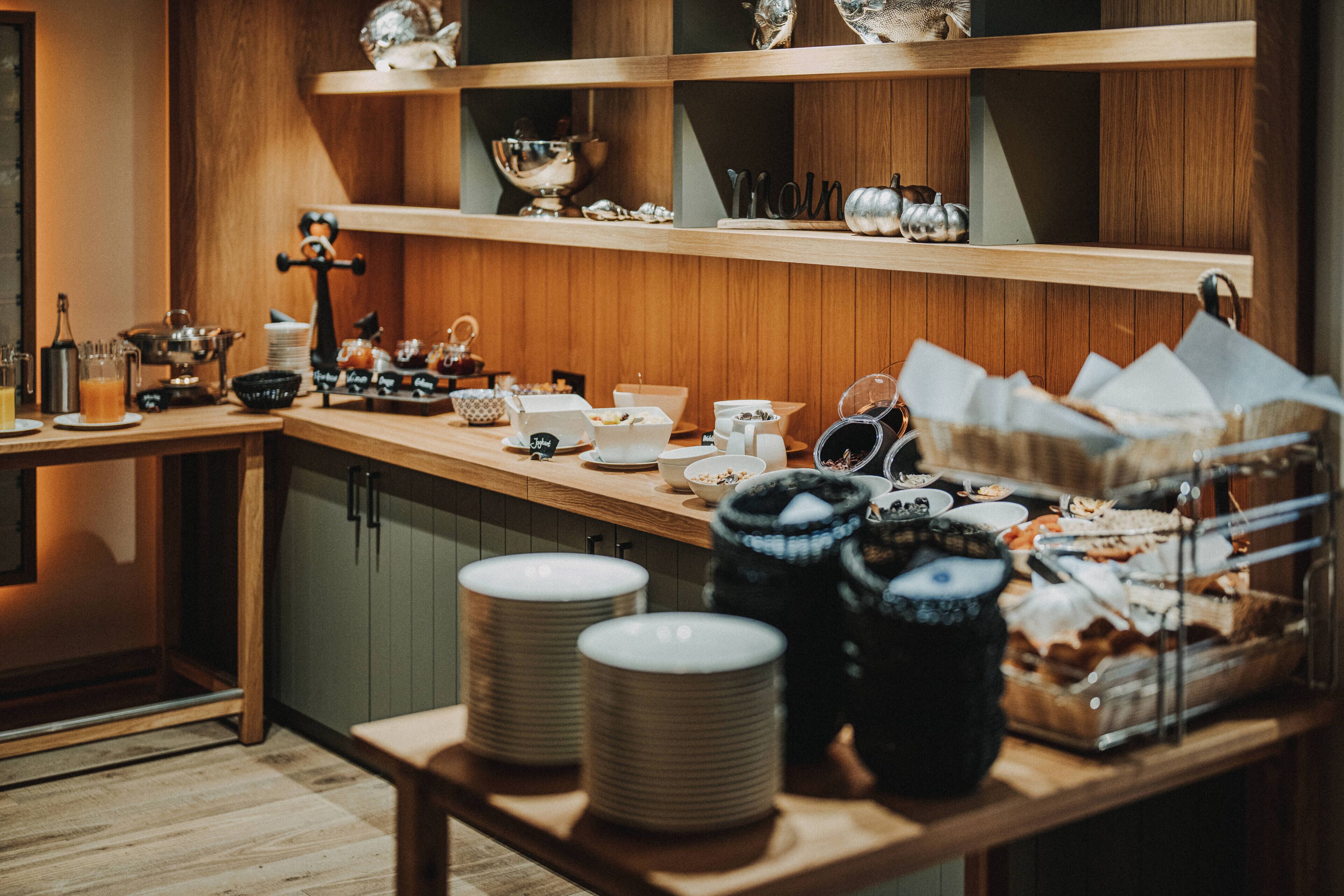 Una cocina con armarios de madera, una encimera con diversos utensilios de cocina y un estante con objetos decorativos.