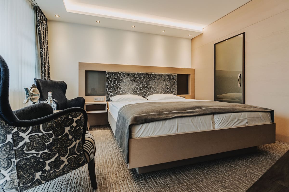 Ett modernt hotellrum med en stor säng, ett nattduksbord, en stol och en stor spegel.