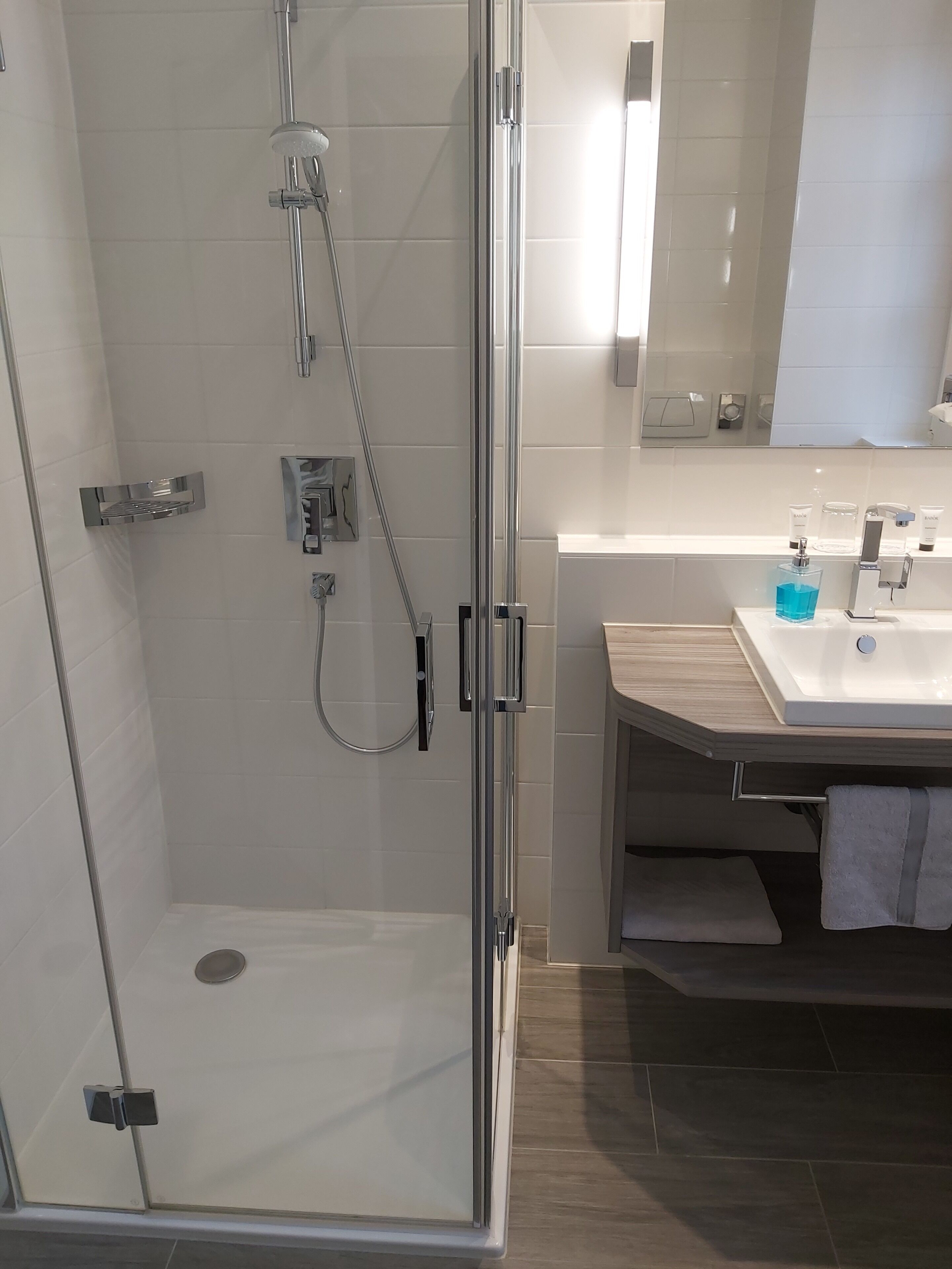 Un bagno moderno con doccia vetrata, mobile bagno in legno e un ampio specchio.