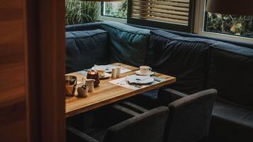 A cozy seating area with a wooden table, cushioned bench, and a window with blinds.