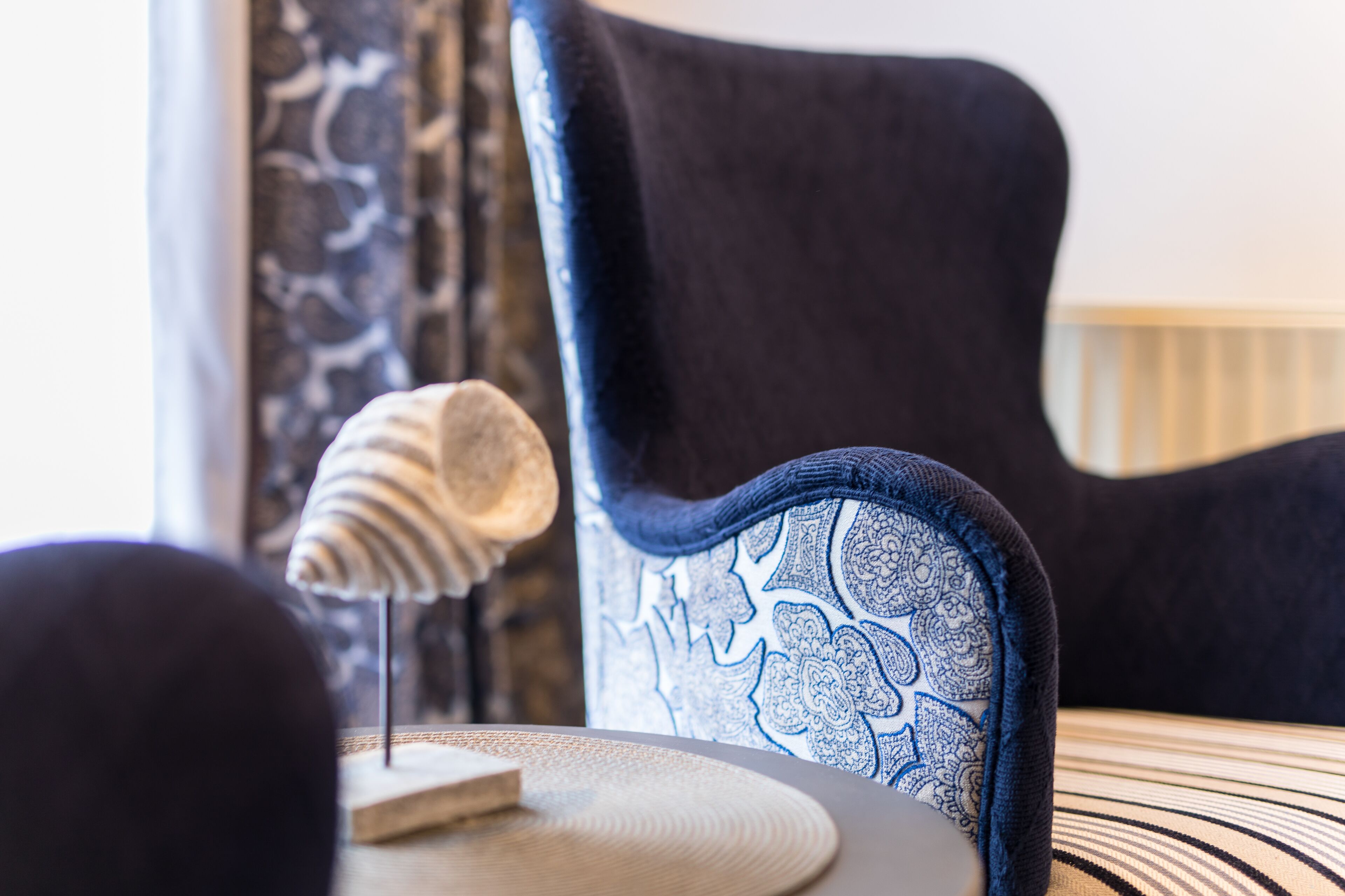 Une chaise avec un dossier à motifs bleus et blancs, une table ronde en osier et un objet décoratif posé sur la table.
