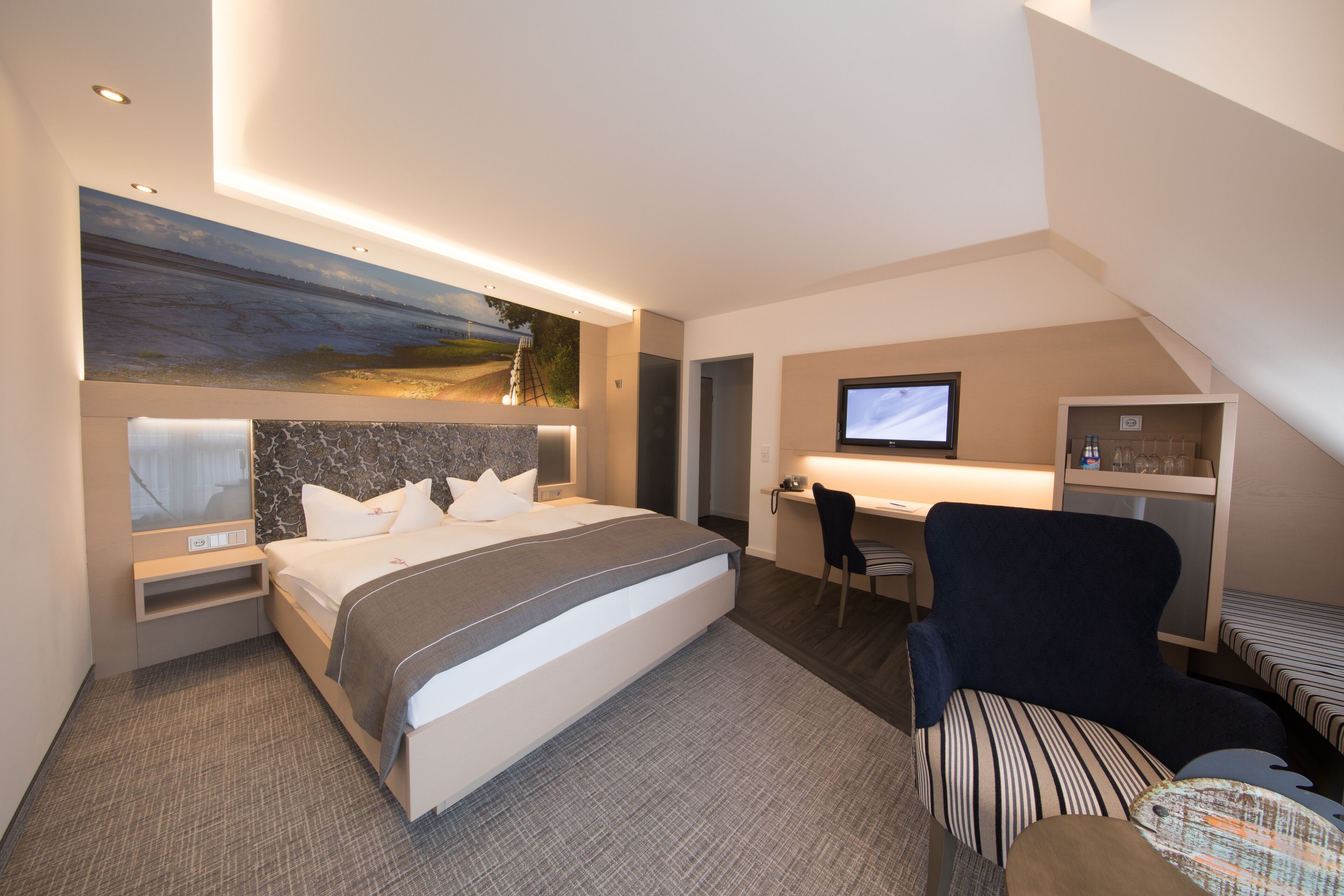 A modern hotel room with a large bed, a desk, a chair, and a TV.