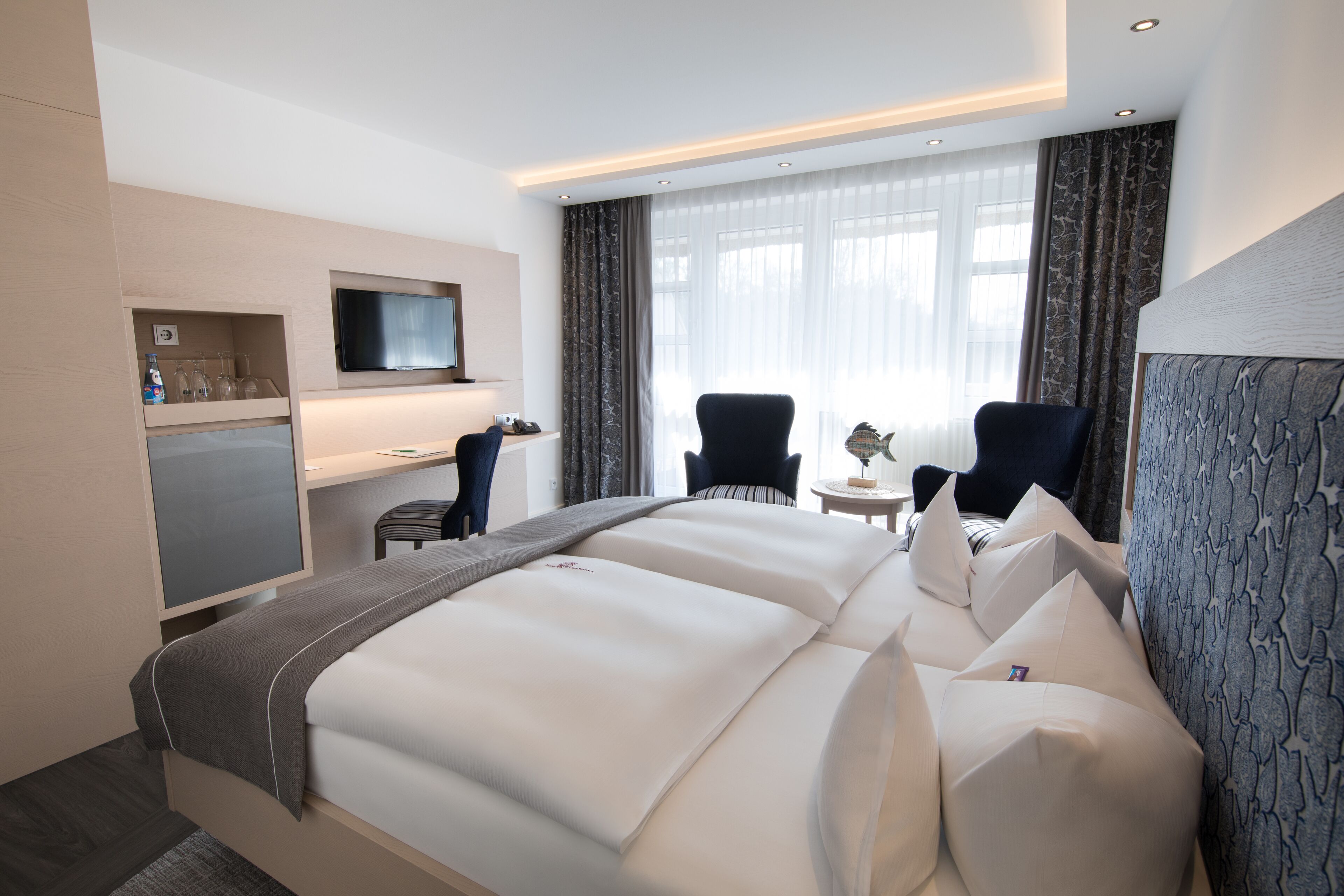 A hotel room with a large bed, two armchairs, a desk, a television, and a minibar.