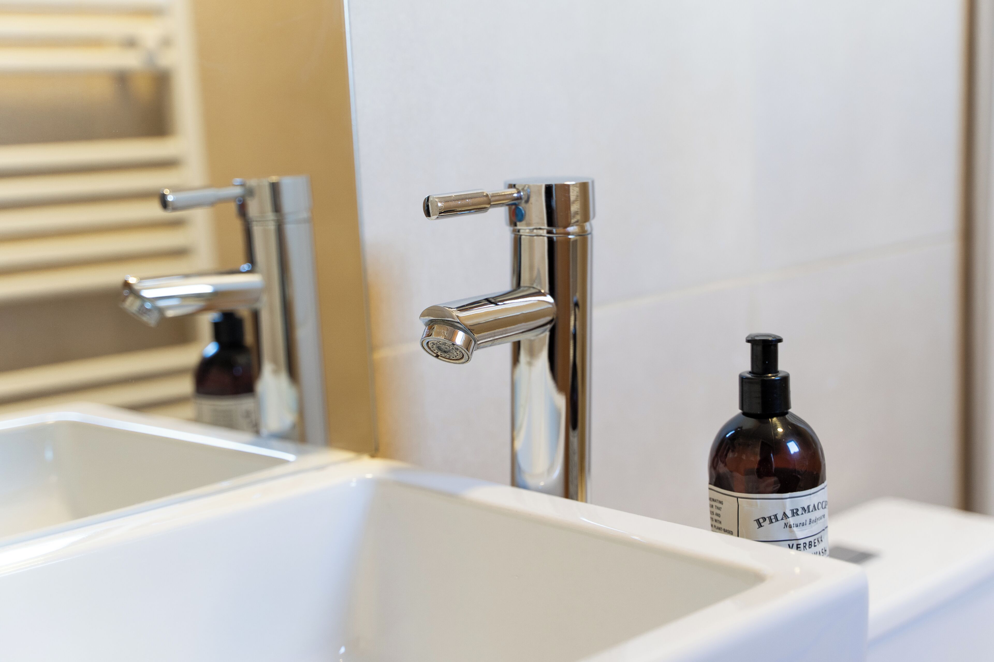Un baño con un lavamanos blanco, grifo cromado y una botella de jabón para manos.