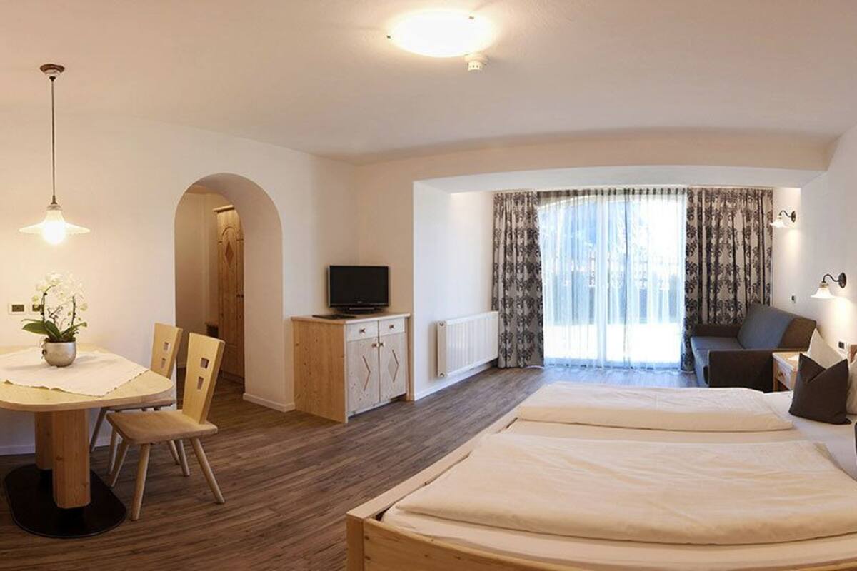 A hotel room with two beds, a desk, a chair, a TV, and a view of the outdoors.