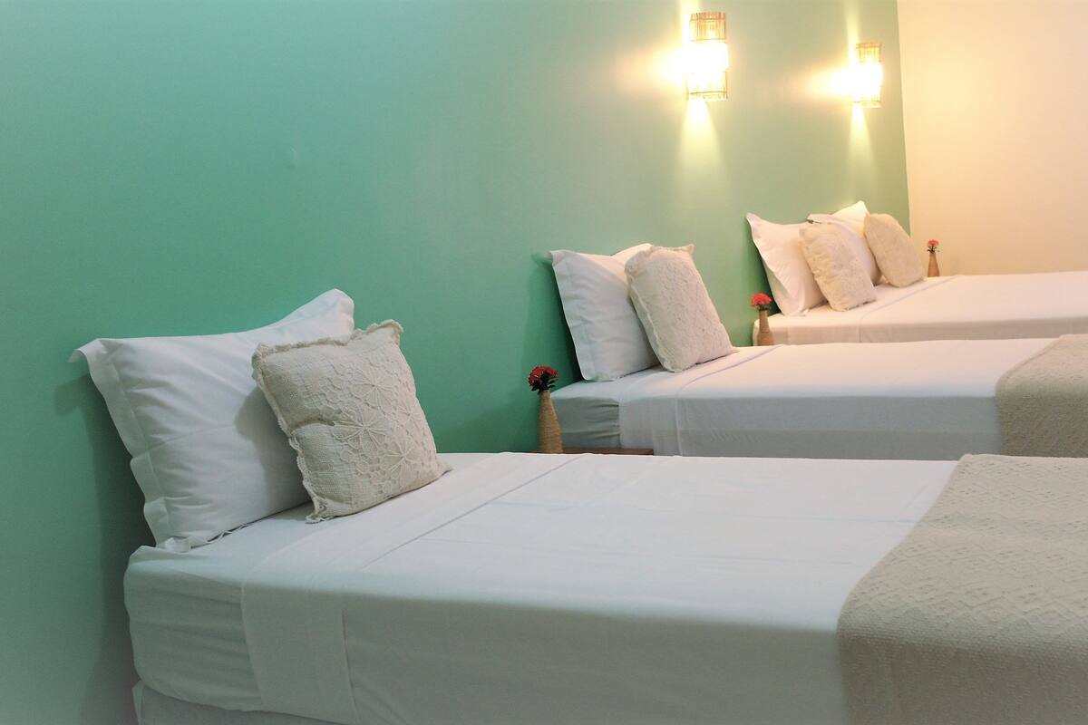 Una habitación de hotel con dos camas, cada una con ropa de cama y almohadas blancas. Hay luces fijadas en la pared sobre las camas.