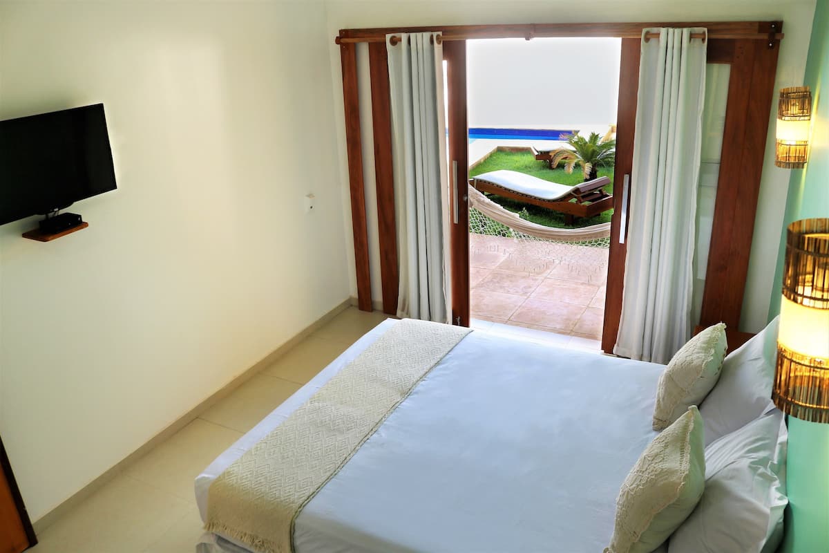 Una habitación de hotel con cama, televisor y vista a una piscina y zona exterior.
