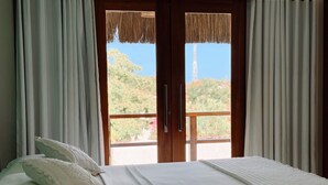Un dormitorio con cama, ropa de cama blanca y vistas a través de un ventanal.