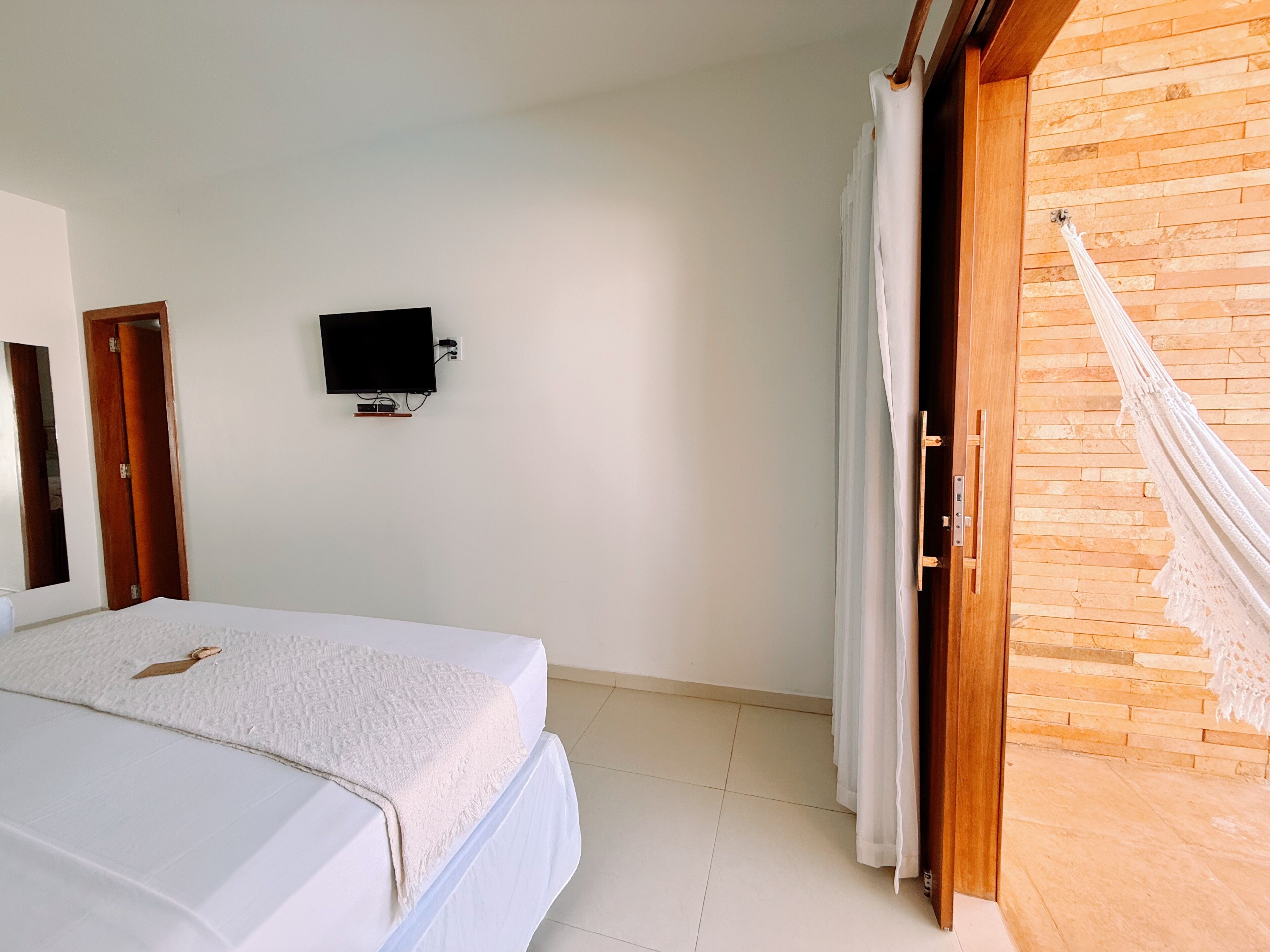 Un dormitorio con cama, televisión montada en la pared y una hamaca.