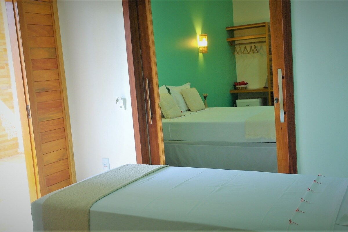 Una habitación con una cama, una mesita de noche, una lámpara de pared y una puerta de madera.