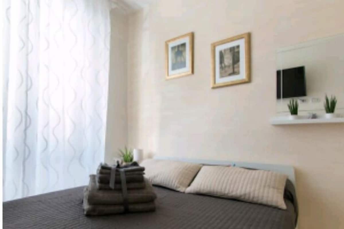 A bedroom with a bed, pillows, a stack of towels, a TV, and two framed pictures on the wall.