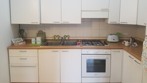 A kitchen with white cabinets, a gas stove, an oven, and a sink. - Retro Apartment (Bergamo)