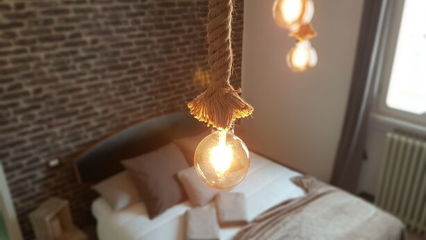 A bedroom with a brick wall, a bed with pillows, and hanging light fixtures. - Retro Apartment (Bergamo)