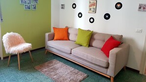 A living room with a beige sofa, two pillows, a fluffy chair, a green wall, and a wall decorated with vinyl records. - Retro Apartment (Bergamo)