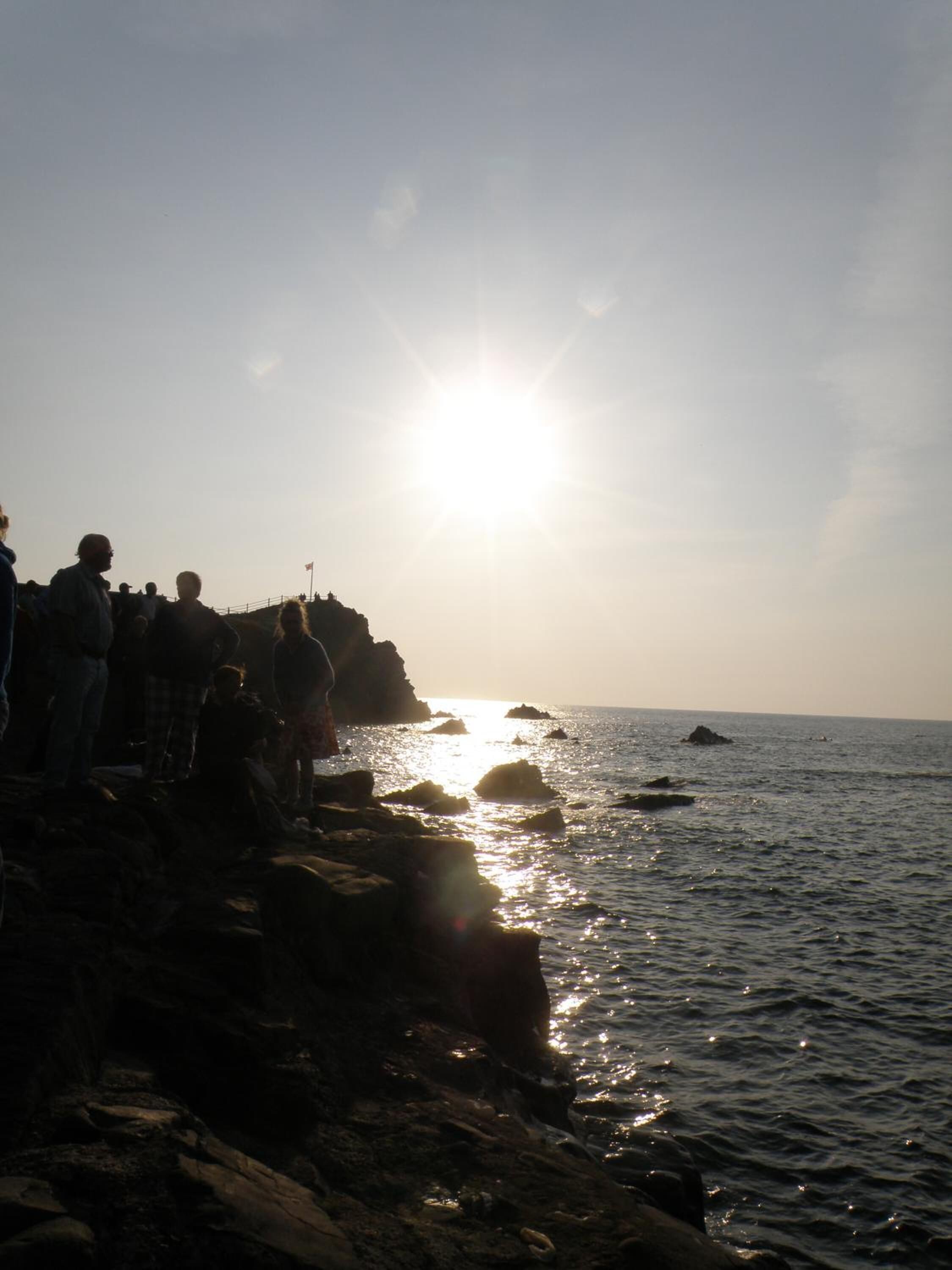 A rocky shoreline with people standing on the edge, overlooking the sea.