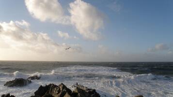 A rocky coastline with waves crashing against the rocks under a partly cloudy sky.