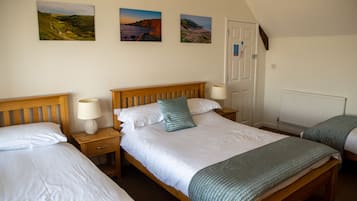 Une chambre avec deux lits simples, une tête de lit en bois, des tables de chevet avec des lampes et trois tableaux représentant des paysages accrochés au mur.