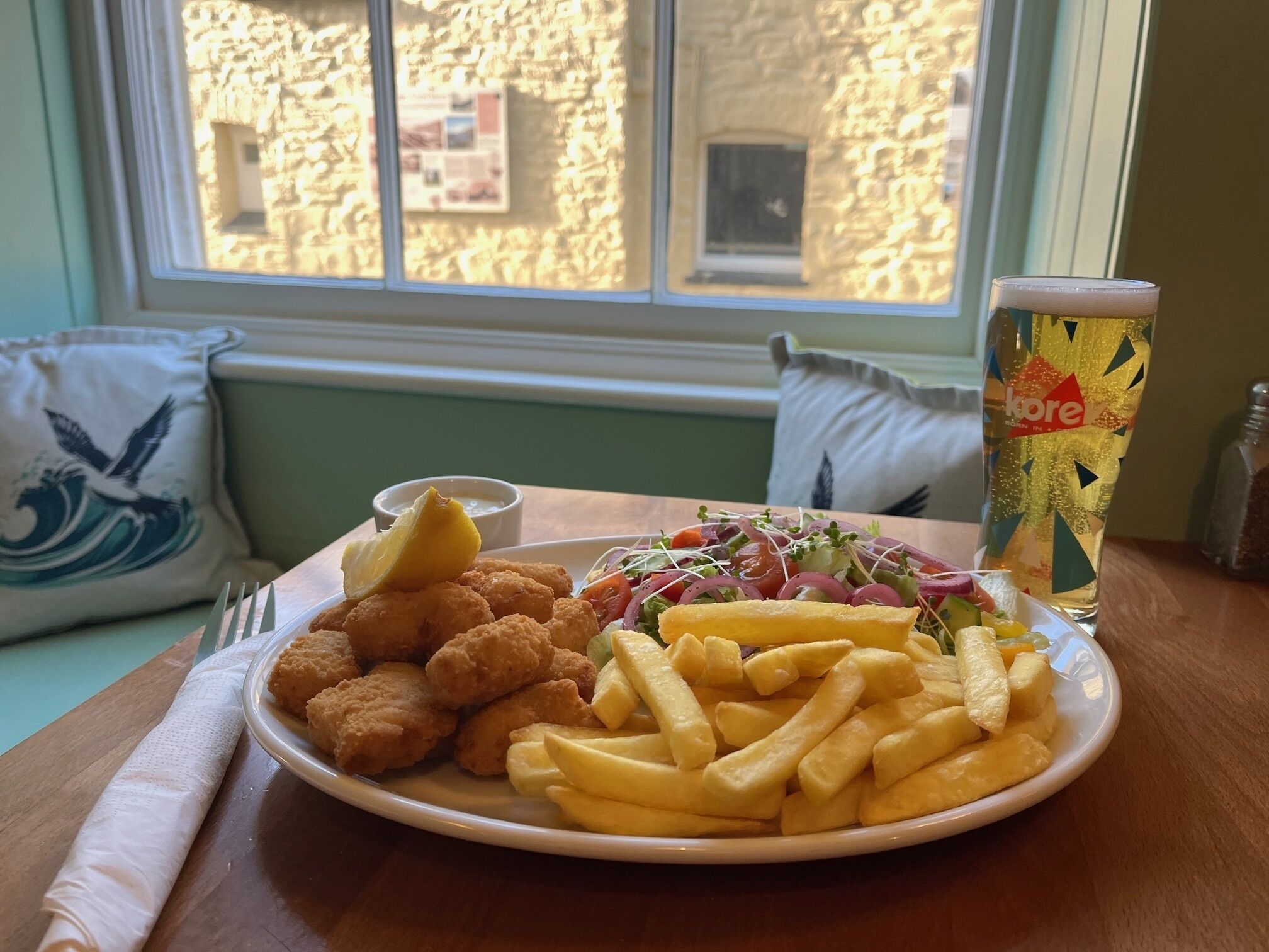 En tallrik med mat som innehåller potatiskroketter, pommes frites och en sallad, samt en dryck i ett färgglatt glas.