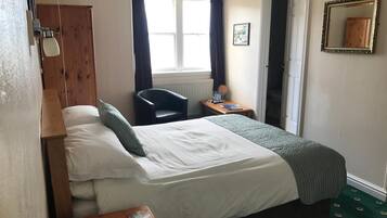 Ein Hotelzimmer mit Bett, Schreibtisch, Stuhl, einem Fenster mit Vorhängen, Heizkörper und Spiegel an der Wand.