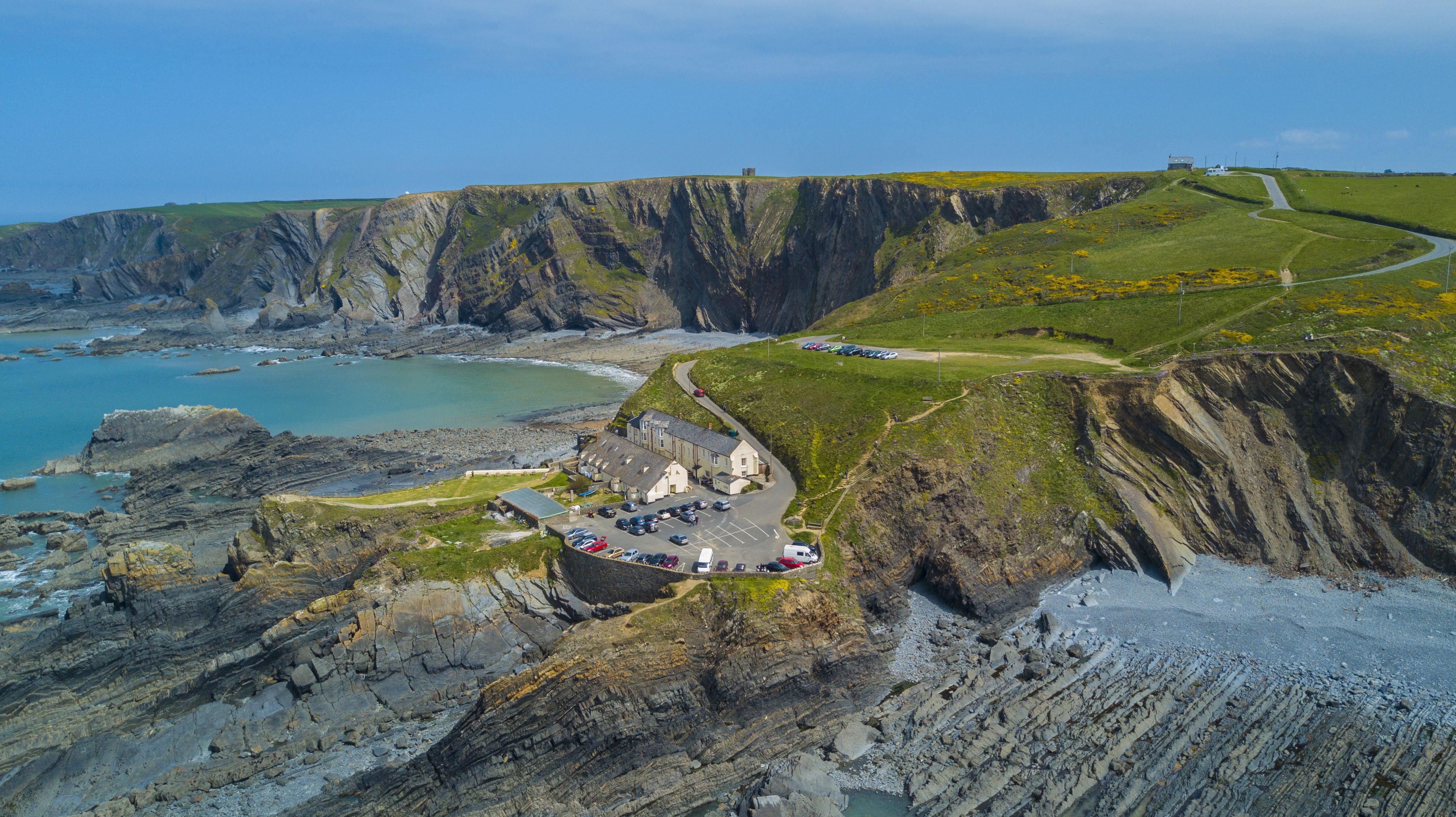 A coastal cliffside with a parking area, buildings, and a road leading to a small settlement.