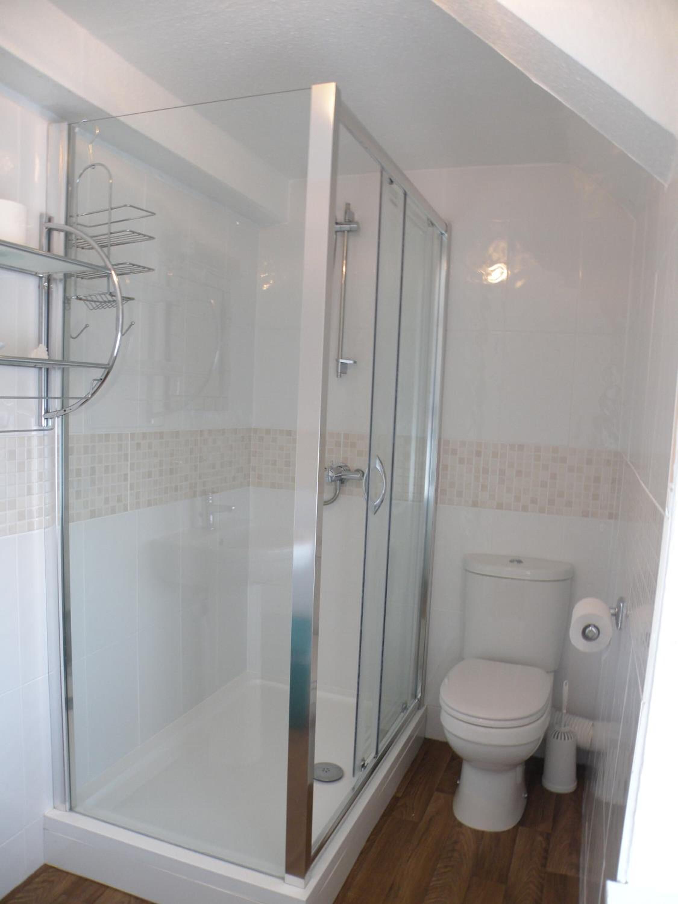 Un baño moderno con ducha envuelta en vidrio, inodoro y un pequeño cubo de basura.
