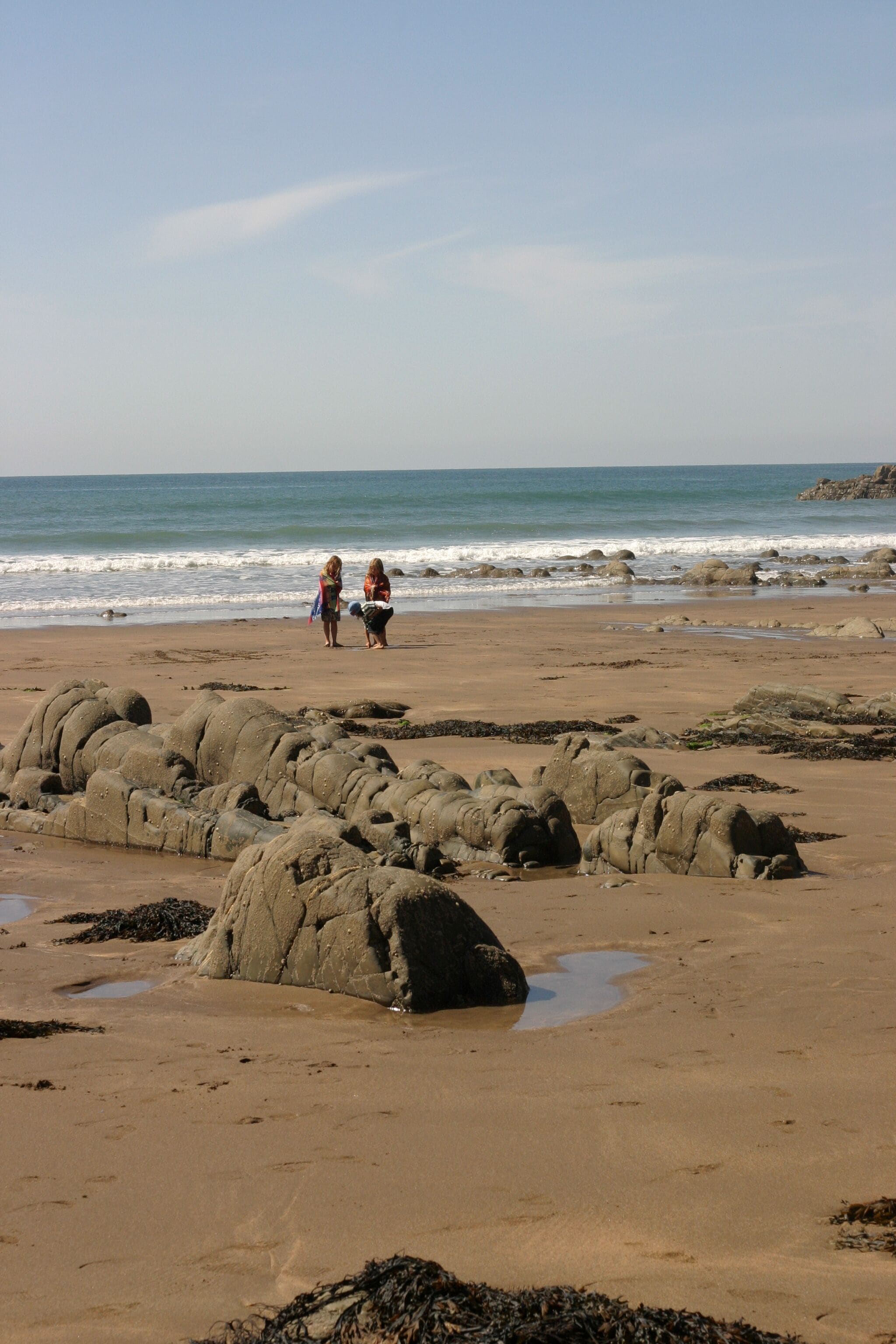 Una playa arenosa con rocas grandes y dos personas a lo lejos.
