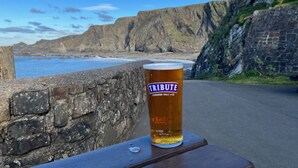Uma cerveja num copo sobre uma mesa de madeira, com vista para o litoral.