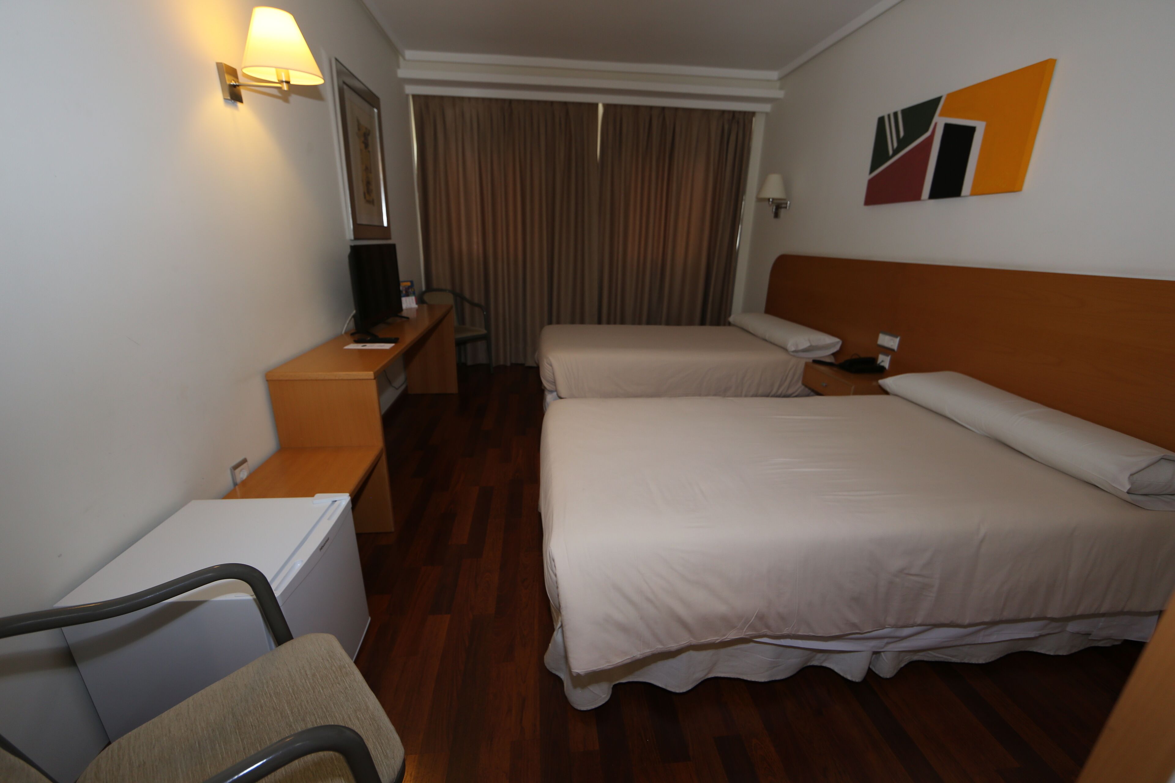 A hotel room with two beds, a desk, a chair, a television, and a curtain.
