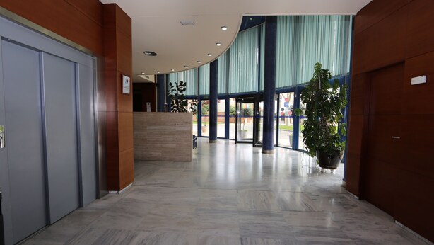 Un vestíbulo amplio con suelo de mármol, una mesa de recepción y ventanas grandes con cortinas azules.