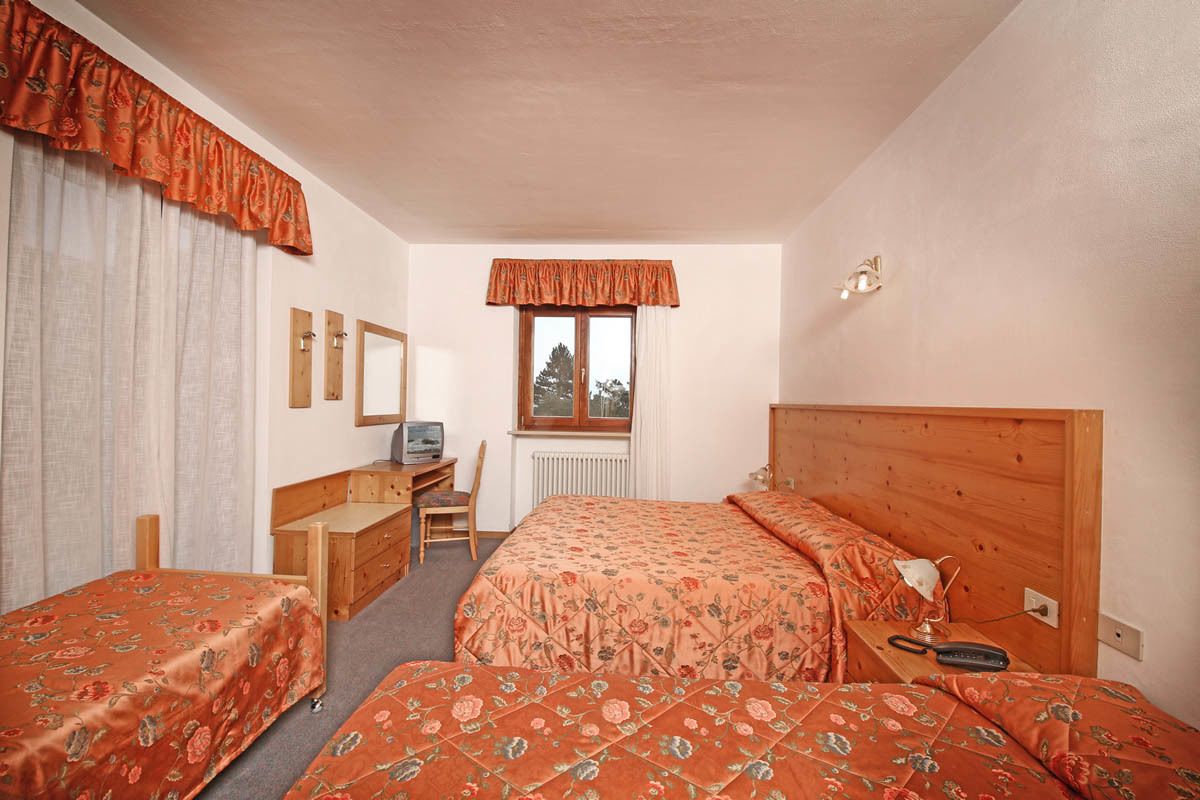 Ein Schlafzimmer mit zwei Einzelbetten, einem Holztisch, einem Stuhl, einem Heizkörper und einem Fenster mit Vorhängen.