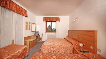 Ein Schlafzimmer mit zwei Einzelbetten, einem Holztisch, einem Stuhl, einem Heizkörper und einem Fenster mit Vorhängen.